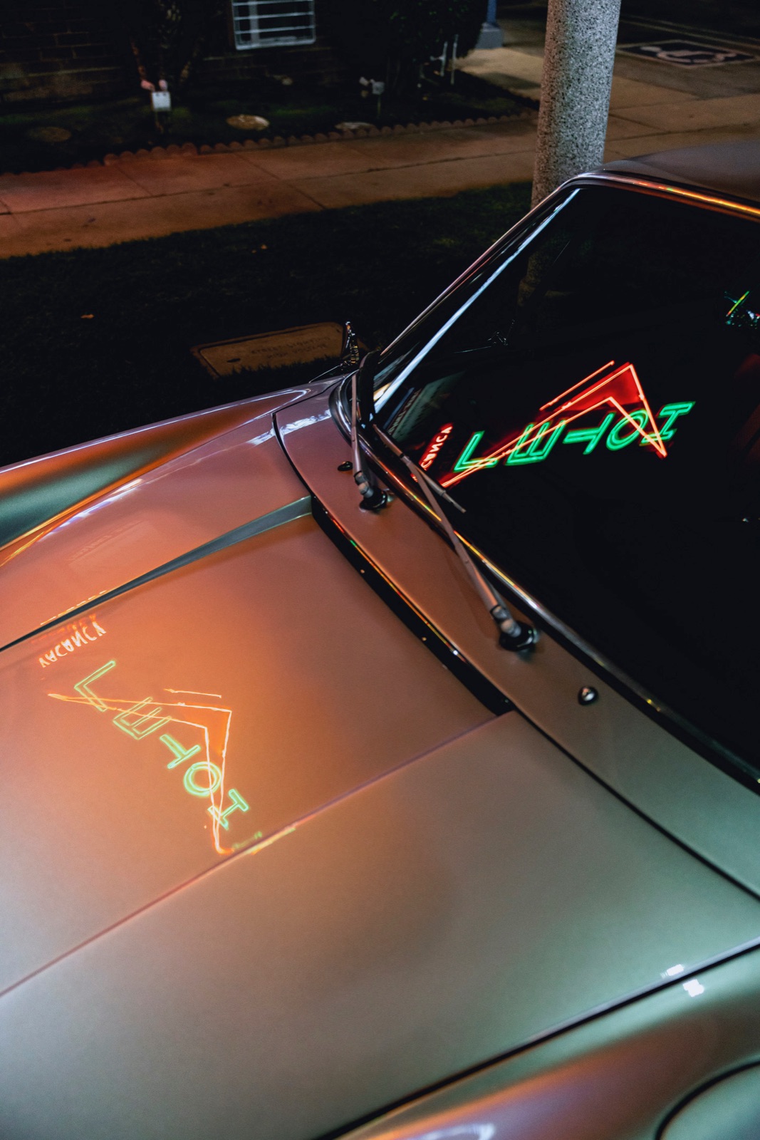 A neon hotel sign reflected across the hood at night